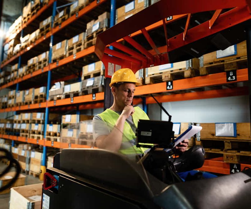 manual-worker-sitting-forklift-reading-paperwork-while-working-warehouse-1