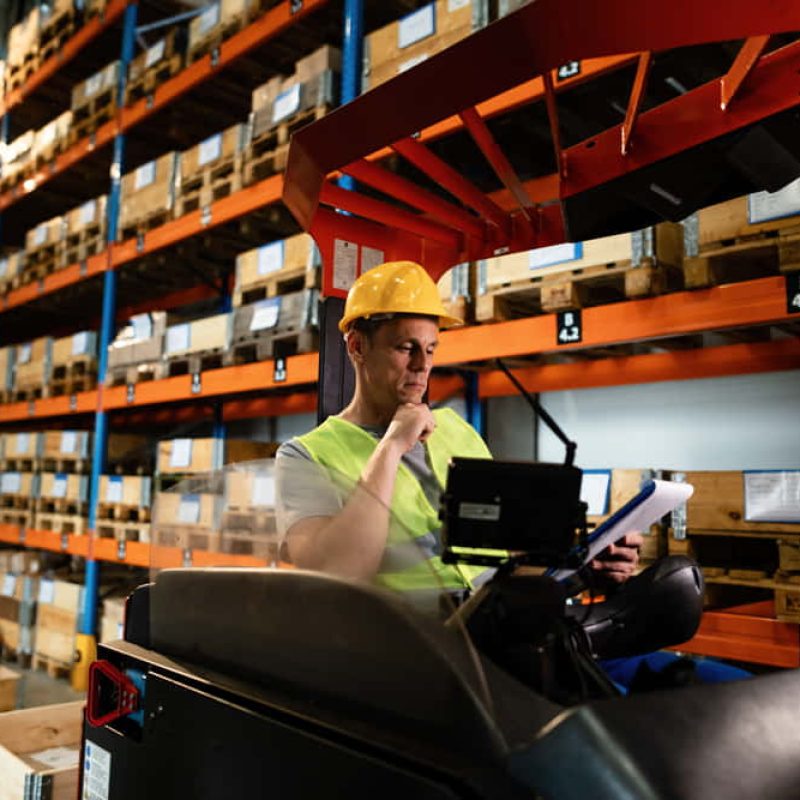 manual-worker-sitting-forklift-reading-paperwork-while-working-warehouse-1